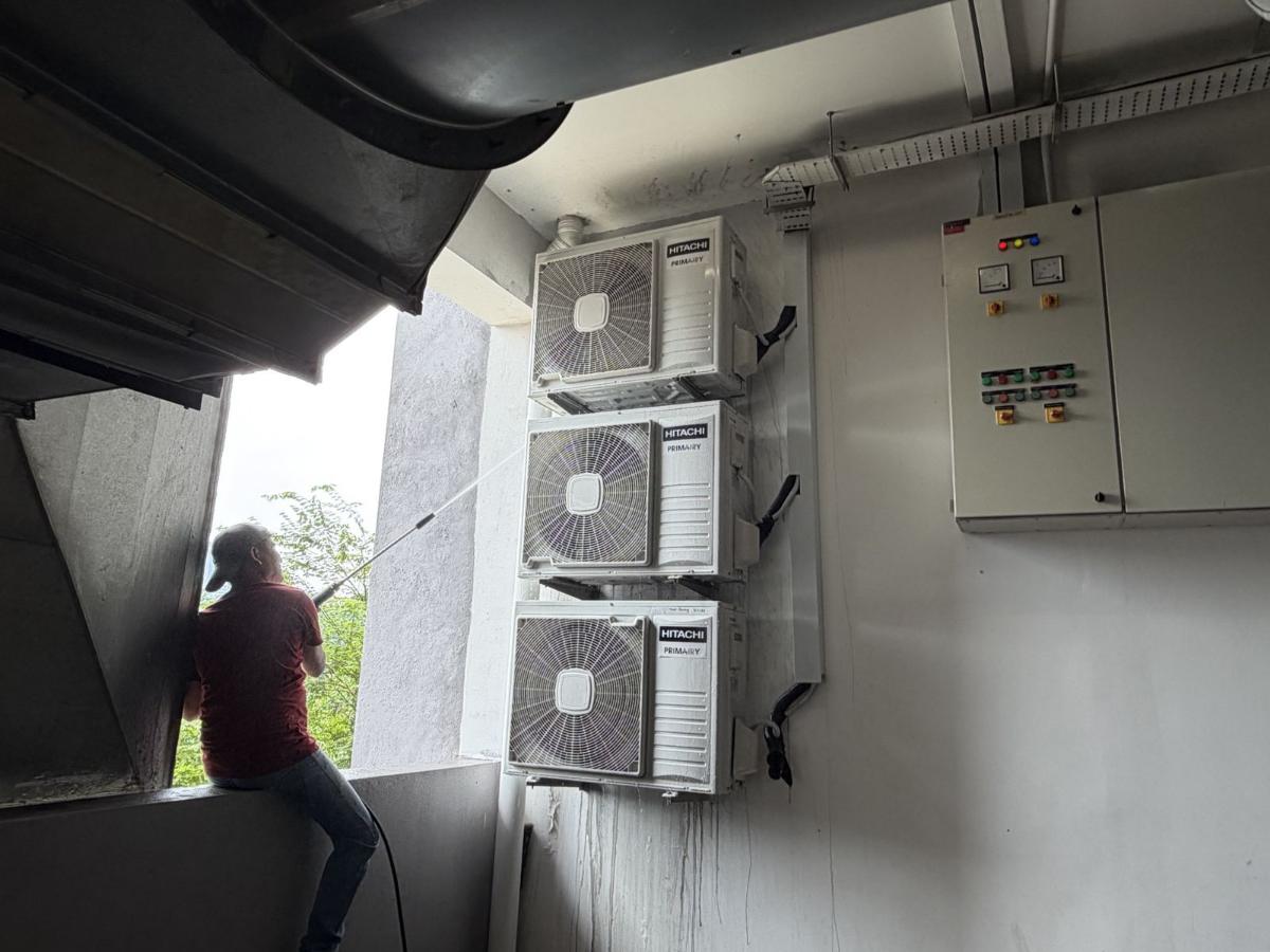 Technician pressure washing three stacked Hitachi outdoor units
